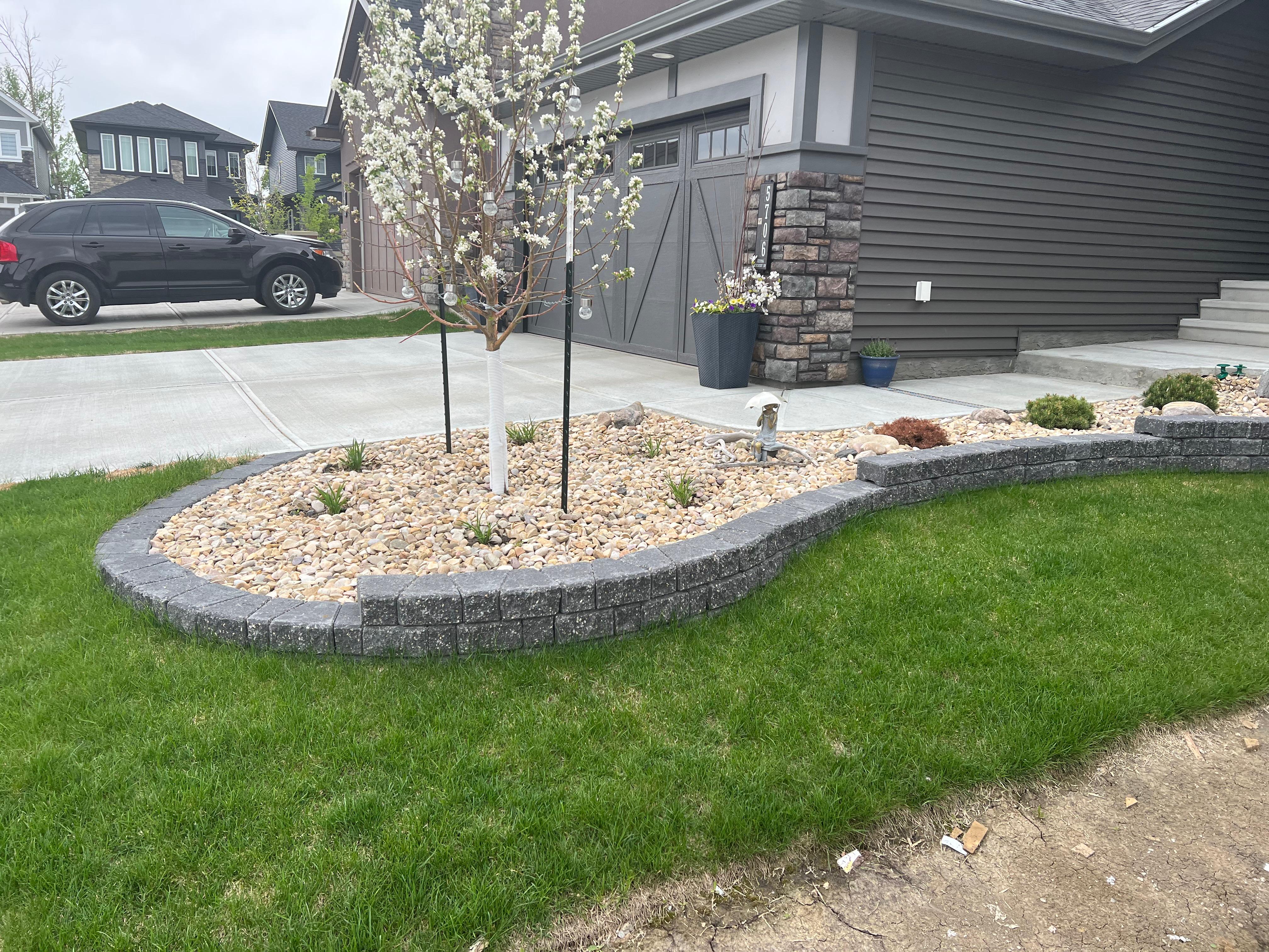 Front yard curved retaining wall with river rock and young flowering tree on green sod